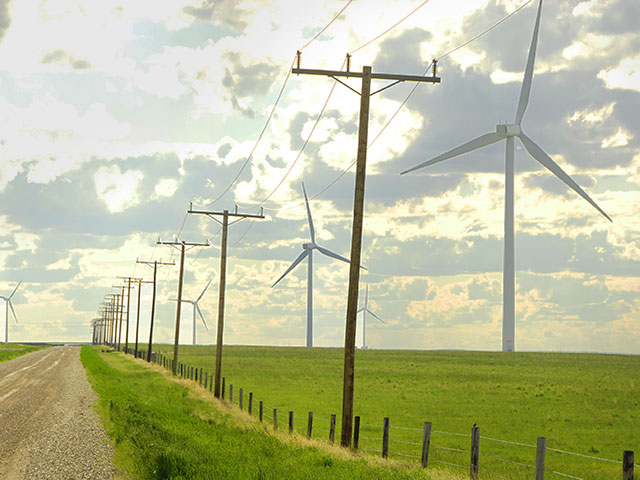 Power poles beside wind turbines in field