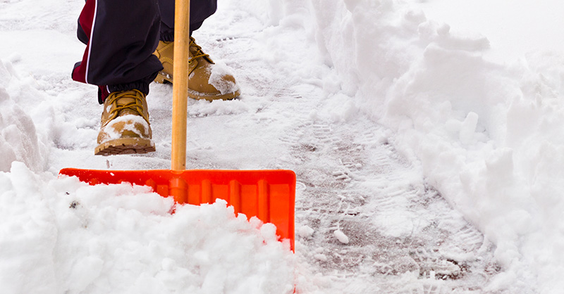 person wearing boots shovelling snow off of a walkway