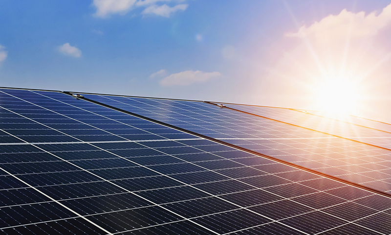 Solar panels in front of a blue sky with the bright sun.