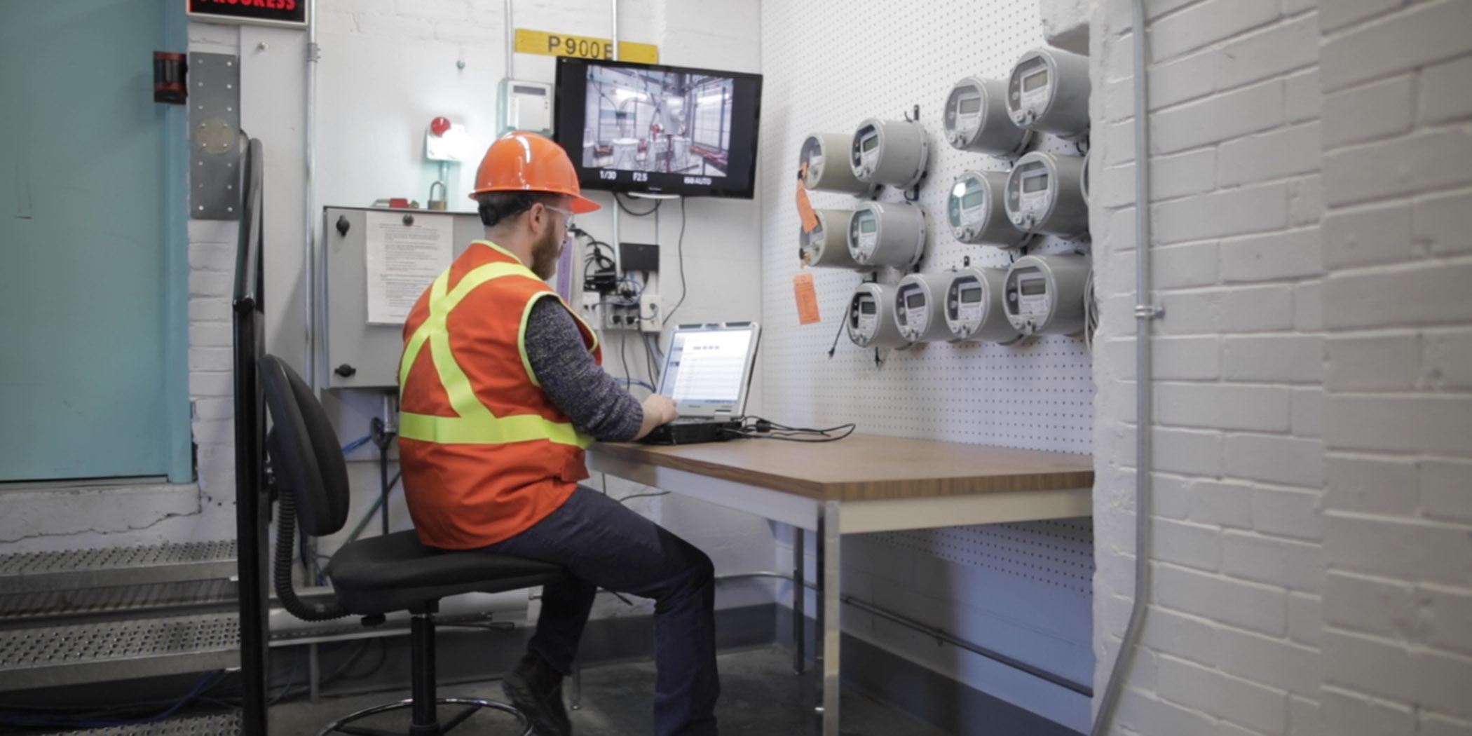 Worker sitting at desk in front of laptop wit smart meters on wall in front of him