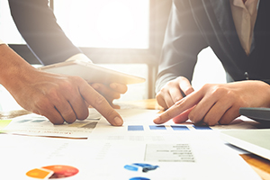 Two people's hands pointing to papers with charts and tables. 