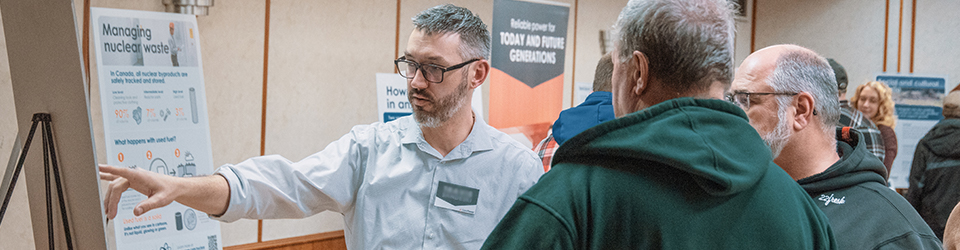 A male pointing to a post board that 2 people are looking at.