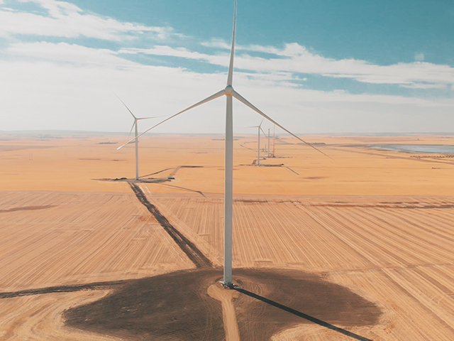 Wind turbines in a field with a blue sky and clouds. 