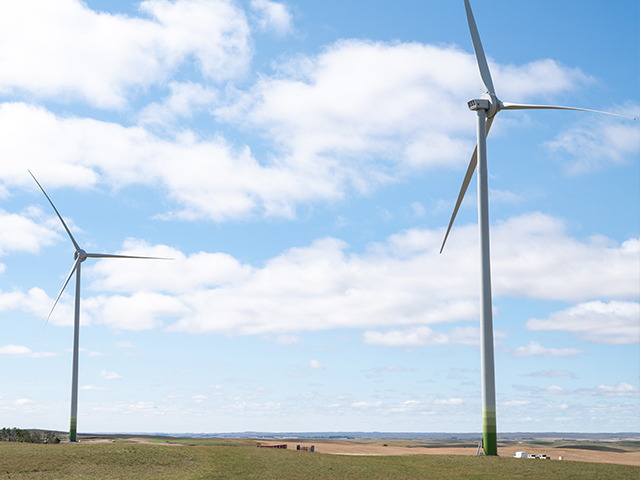 Two large wind turbines with a blue sky and clouds behind. 